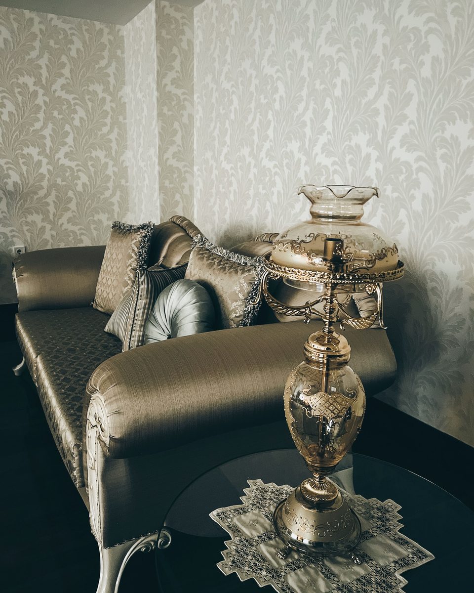Sitting room corner with a tone-on-tone ivory damask wallpaper, a silk chaise and a cut-glass oil lamp