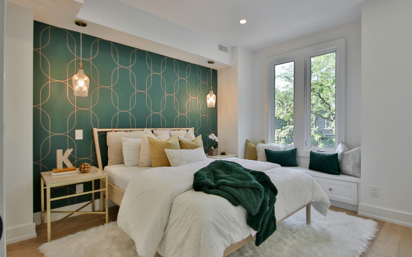 Bright bedroom with a deep green geometric feature wall behind the bed, pendant lights and a cushioned window seat