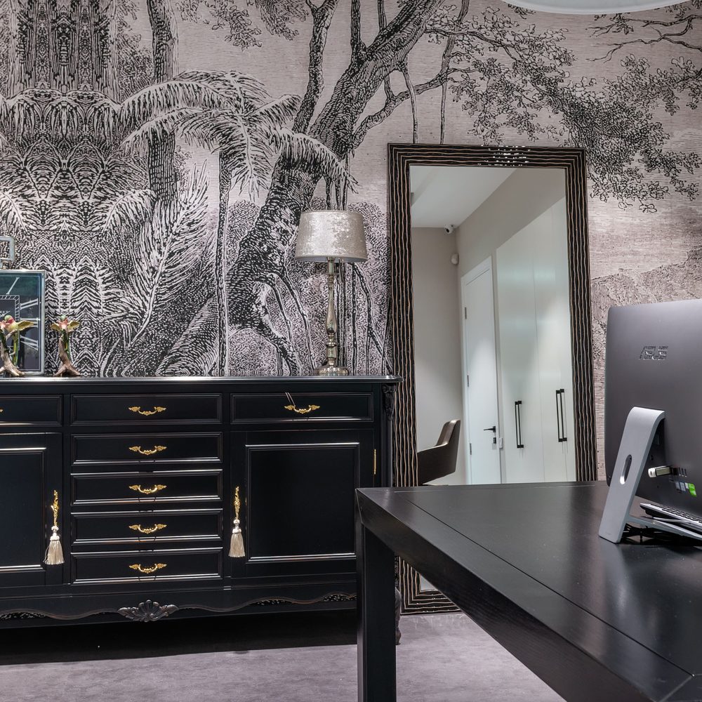 Home office with a monochrome engraved-forest mural wallcovering behind a black sideboard and desk