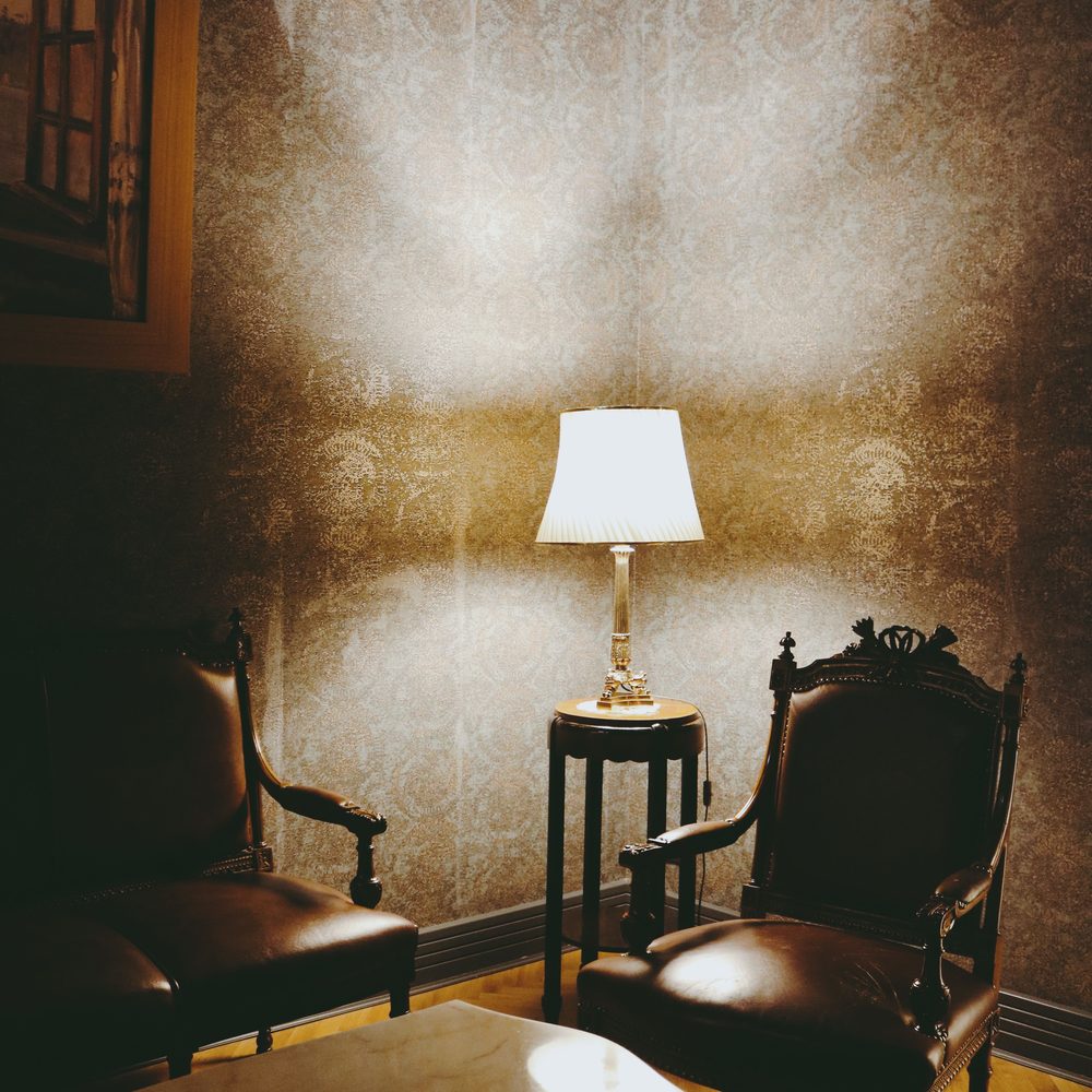 Traditional sitting corner with two carved leather armchairs and a table lamp glowing against a textured patterned wallpaper