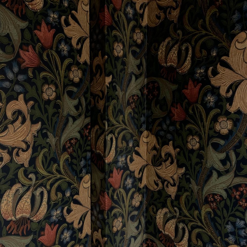 Close-up of a classic Arts and Crafts style wallpaper with lilies and leaves in gold, rust and green on a dark ground