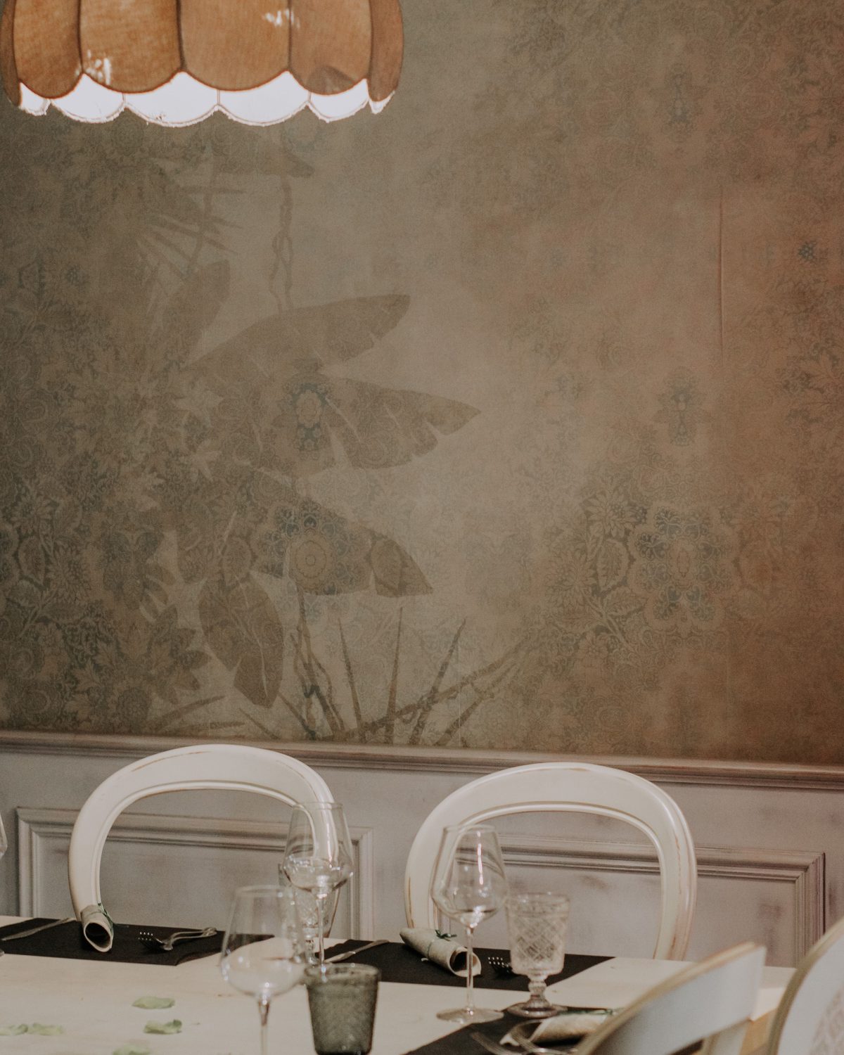 Dining room with a soft botanical wallcovering above white paneled wainscoting, a table set beneath a scalloped pendant